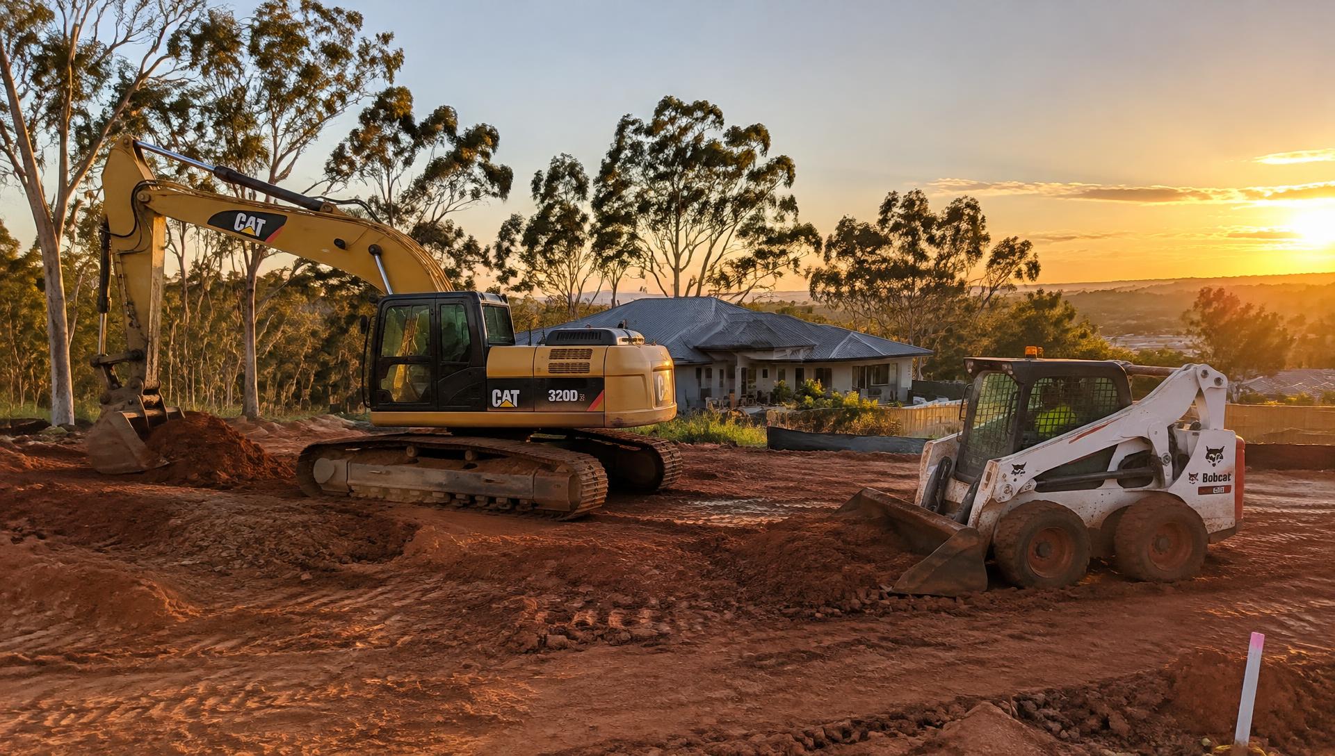 Excavator and bobcat on a residential site in Logan at sunset